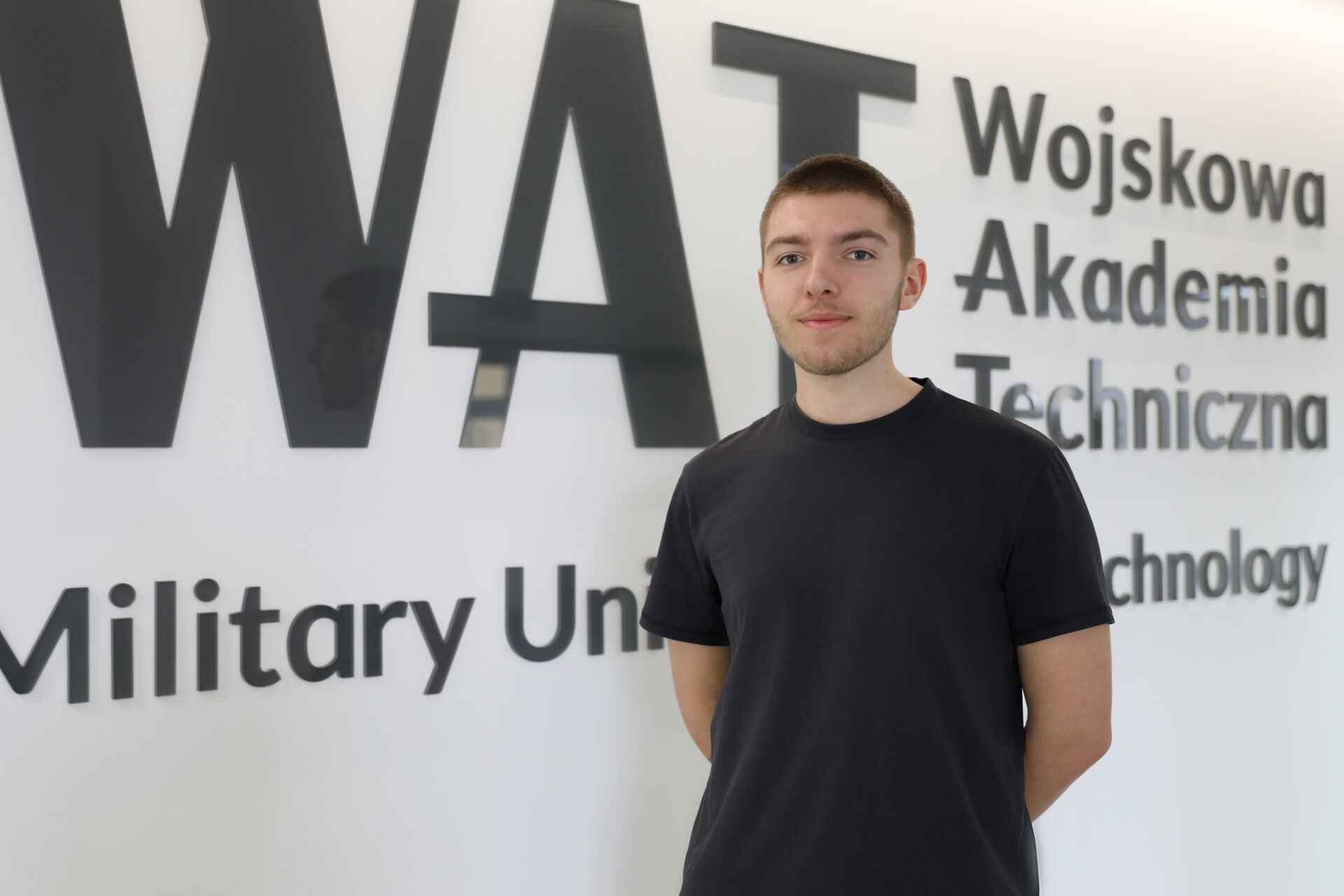 Mateusz Kiersnowski na tle logotypu WAT